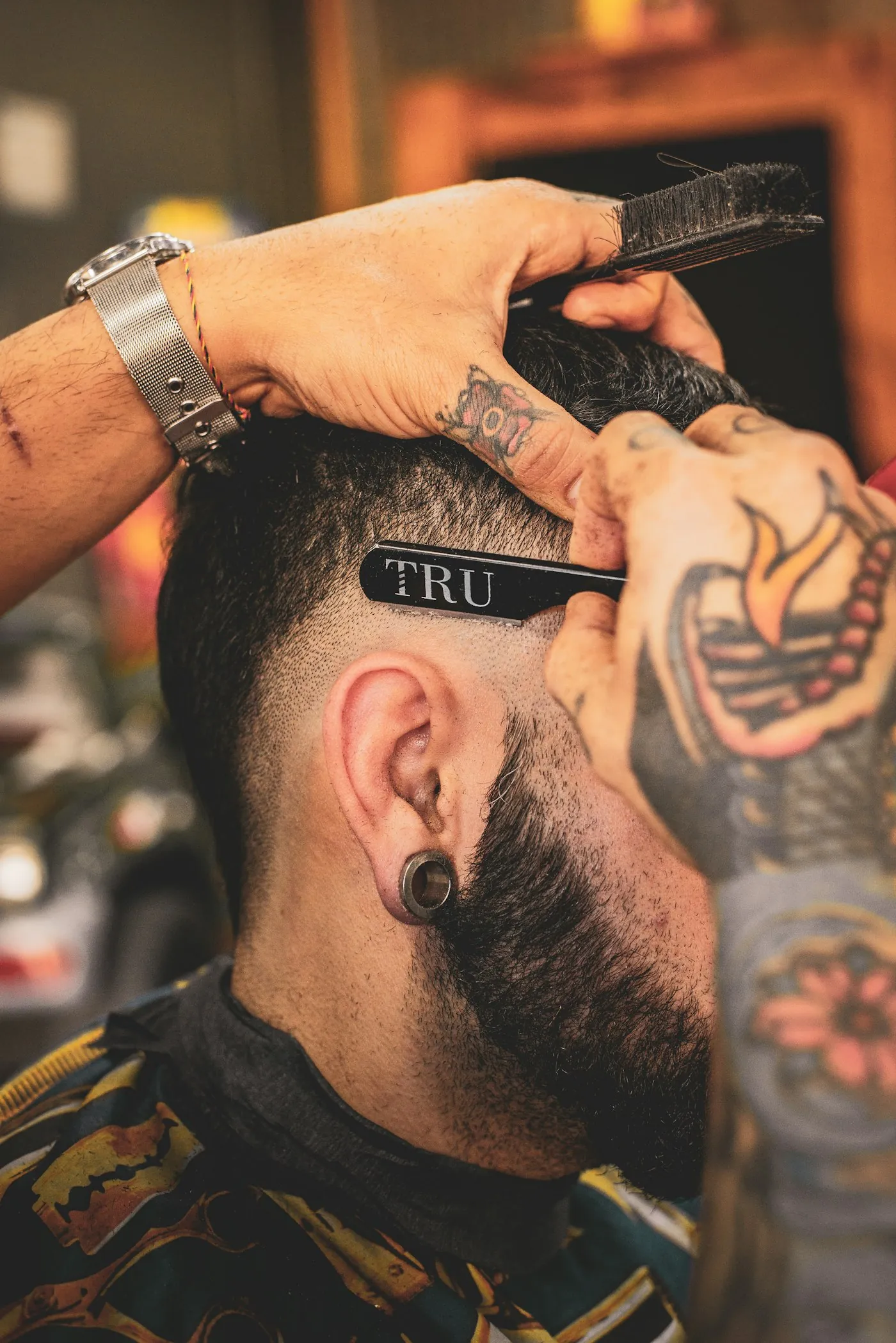 Barbeiro tatuado aparando a barba de um cliente